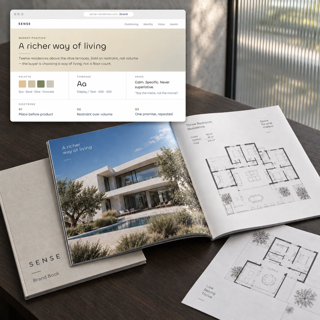 A developer’s market preparation on one desk: the brand platform page with positioning, palette, typeface and voice, an open project brochure with the facade and a floor plan, and a printed plan sheet